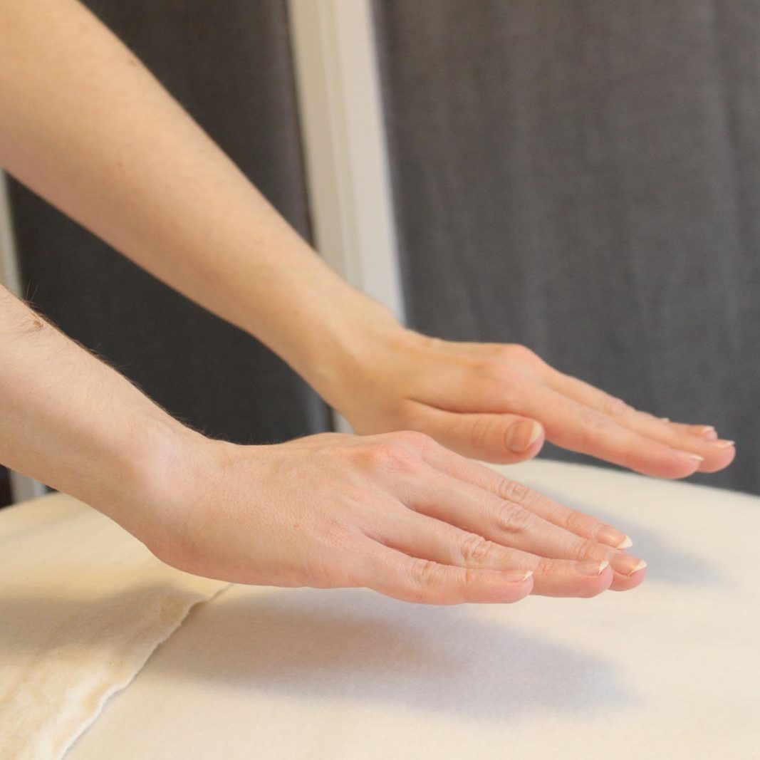 Reiki wird über die Hände übertragen Die Hände der Reiki-Meisterin sind zu sehen, wie sie sie über eine weiße Decke hält und dabei Reiki überträgt.